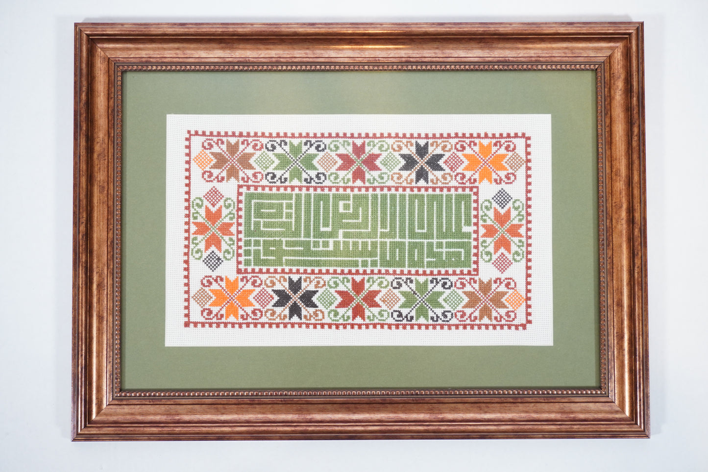 Handmade Palestinian tatreez framed artwork with “على هذه الأرض ما يستحق الحياة” (On this land, there is what deserves life), floral embroidery in orange, green, and black, symbolizing hope, beauty, and homeland