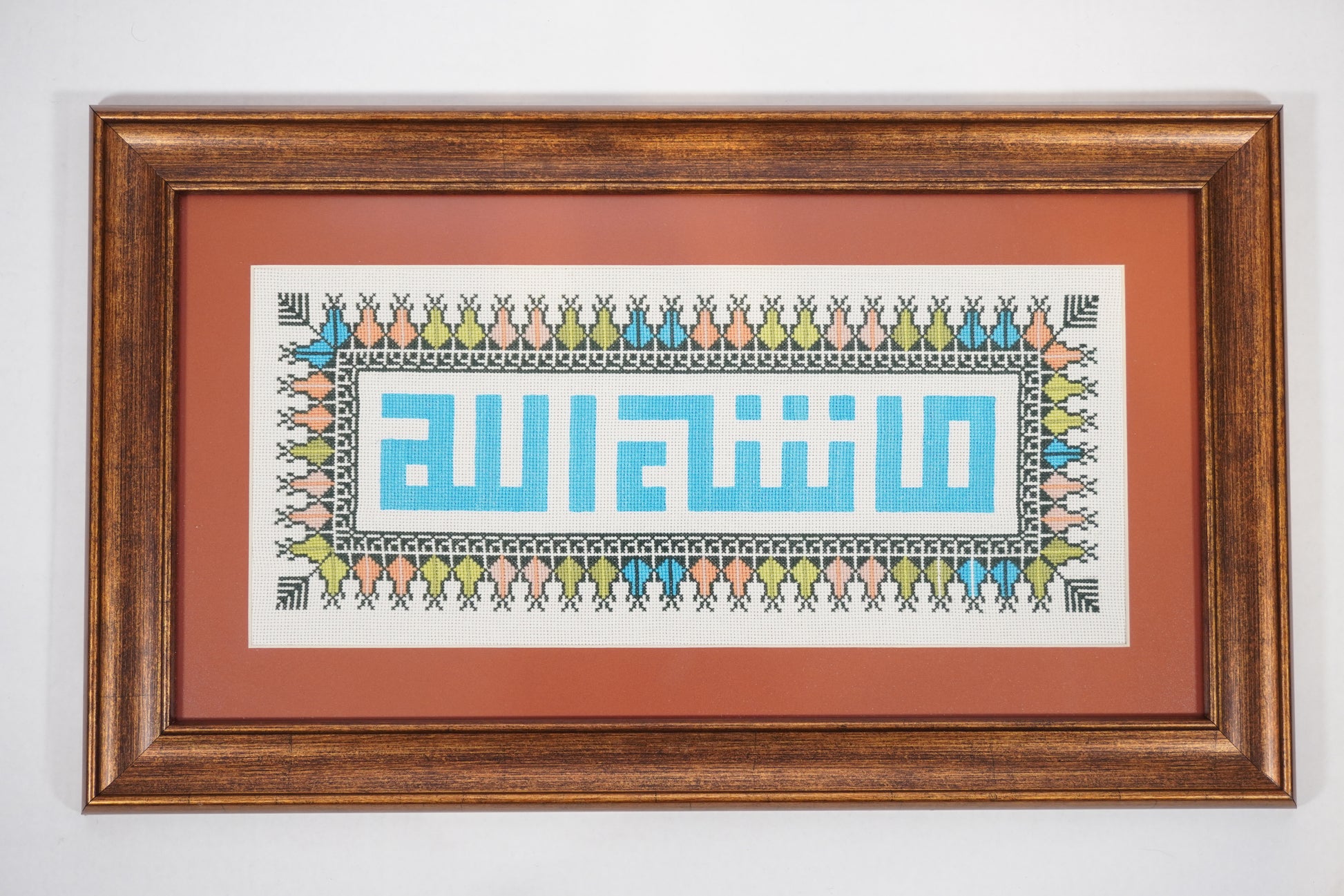 Handmade Palestinian tatreez framed artwork with “ما شاء الله” (What God has willed) in blue embroidery, surrounded by colorful floral patterns, Islamic home decor