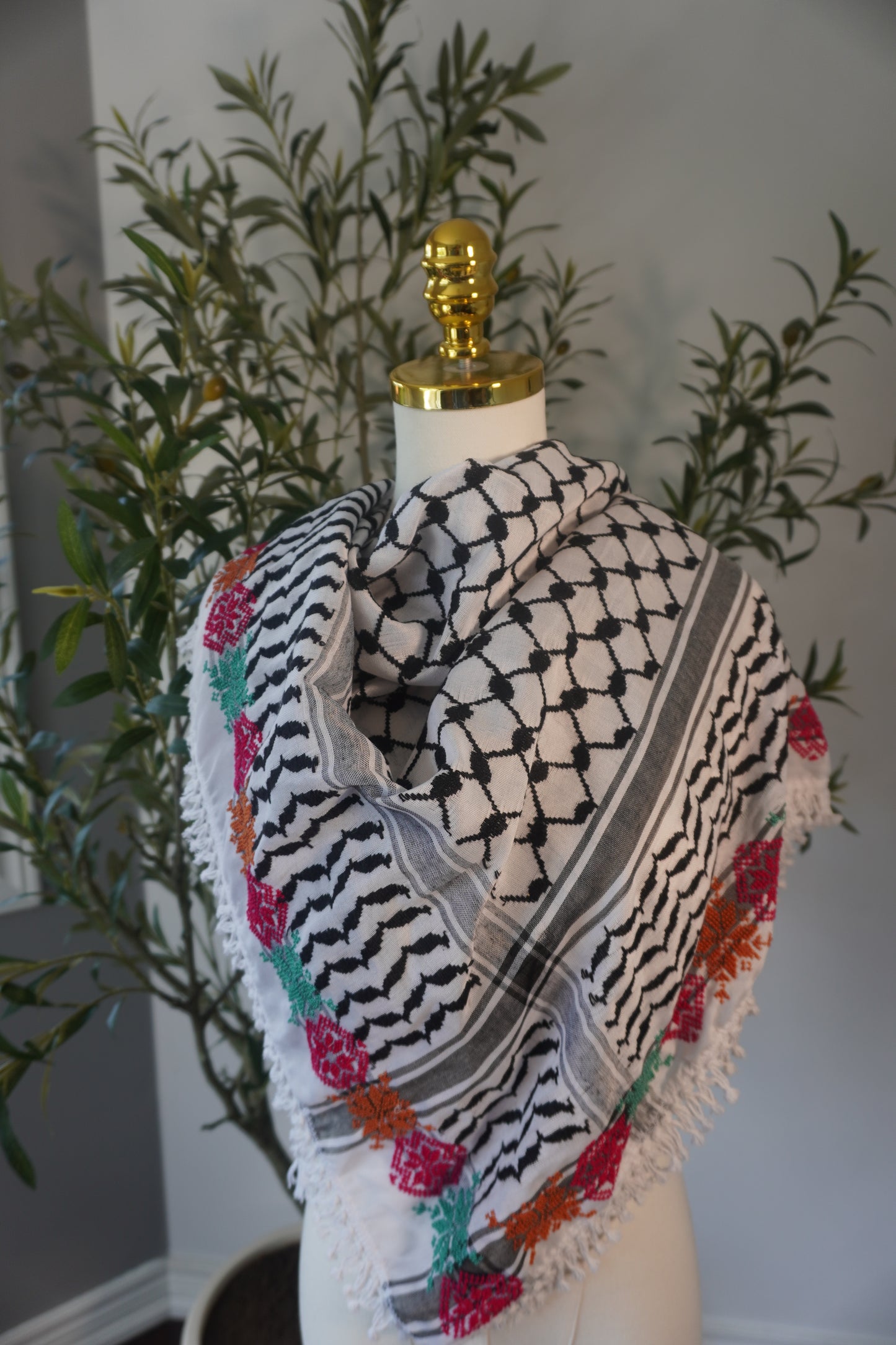A handmade black and white kofea adorned with intricate tatreez embroidery in vibrant light green, pink, and orange, showcasing exceptional craftsmanship and a blend of traditional and contemporary style.