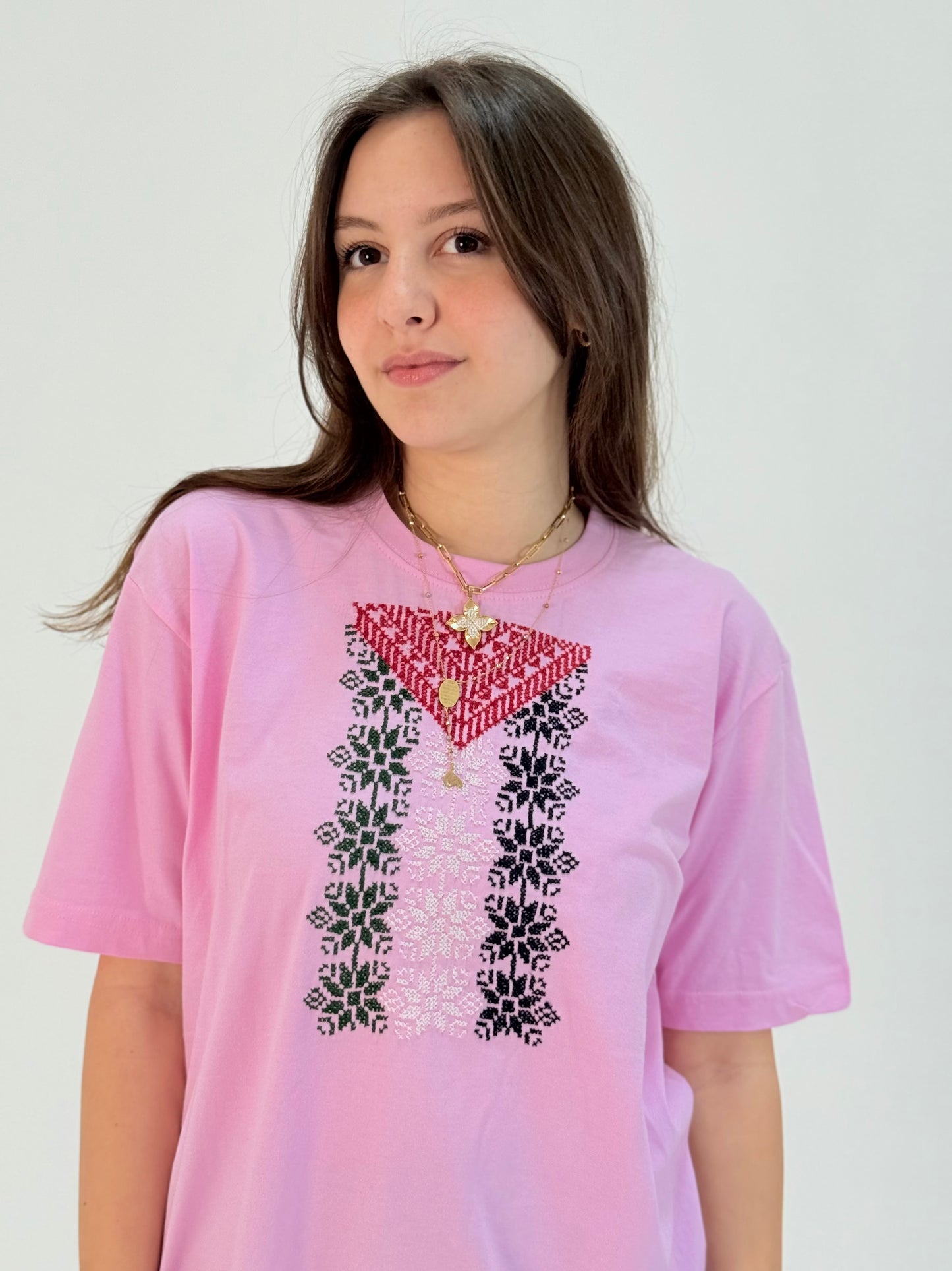 Pink cotton t-shirt featuring hand-embroidered Palestinian flag colors in traditional tatreez pattern, youth cultural heritage wear