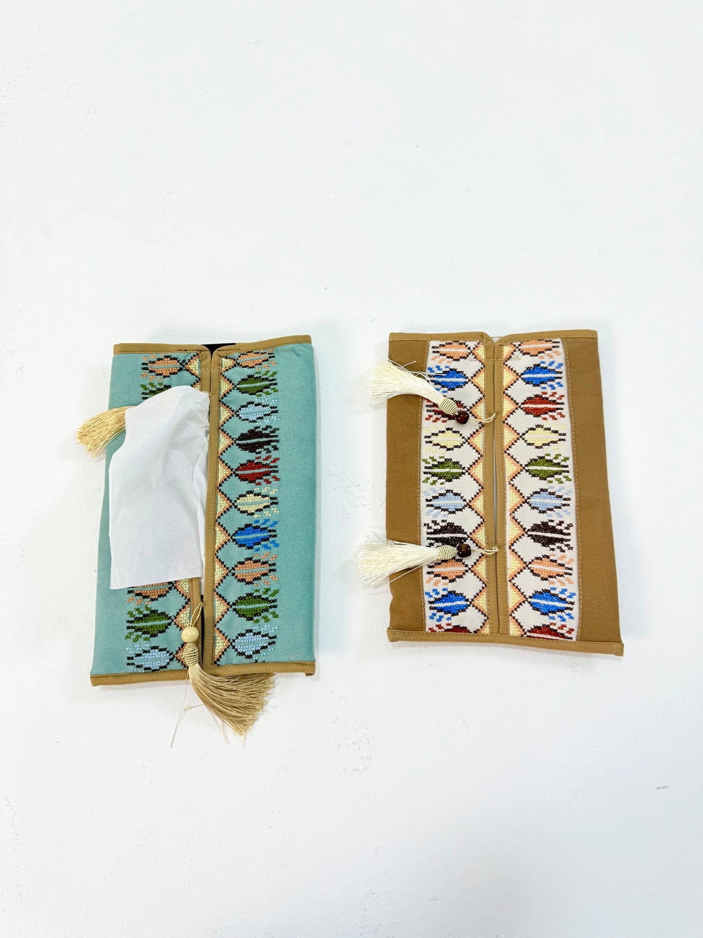 Hand-embroidered suede tissue box covers with vibrant Palestinian tatreez geometric patterns and tassel details, adding warmth and elegance to living spaces, handmade by women artisans from Palestine and Jordan.