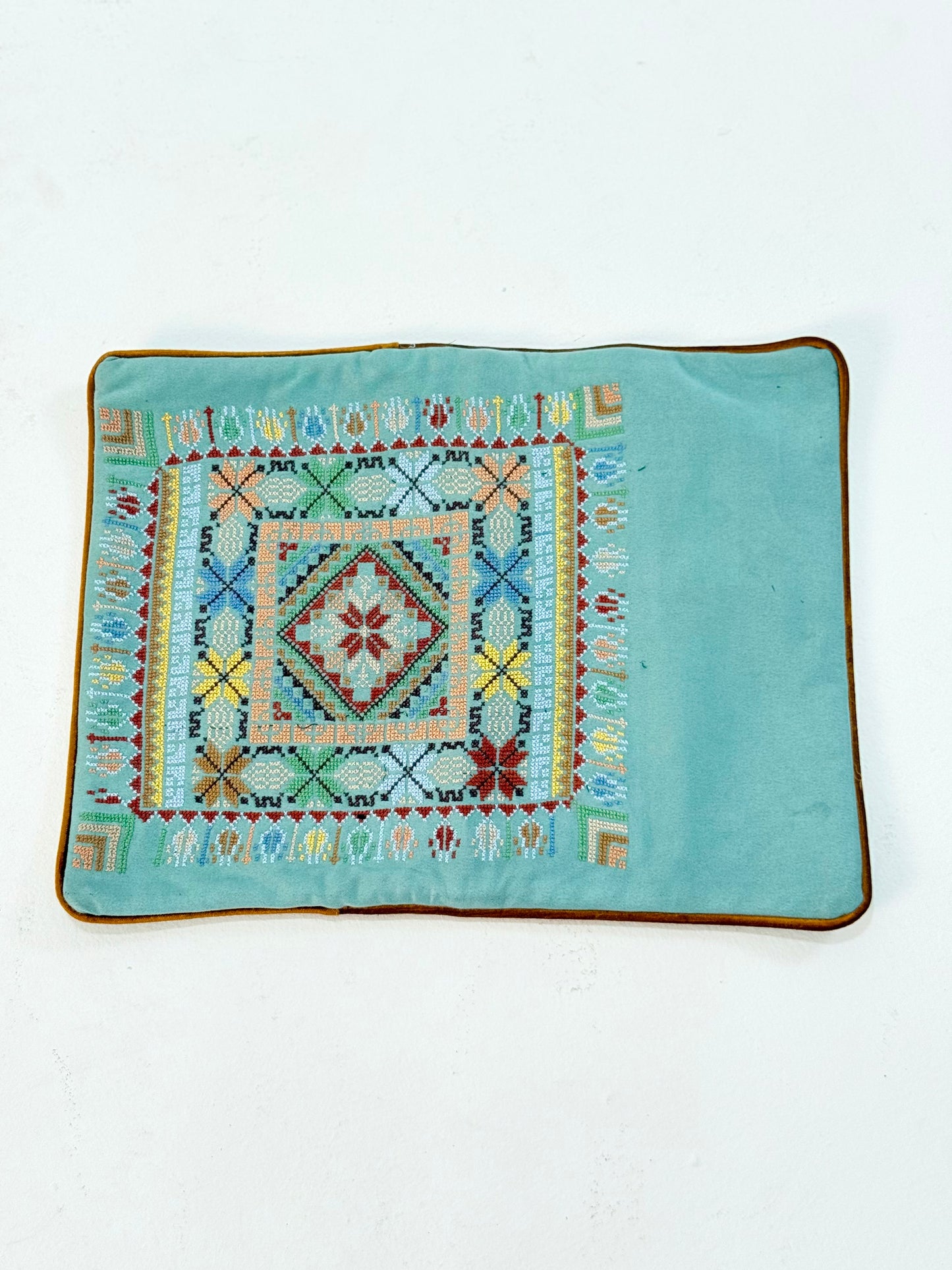 Hand-embroidered rectangular cushion covers featuring vibrant Palestinian tatreez geometric motifs on beige and turquoise backgrounds, crafted by women artisans from Palestine and Jordan to preserve heritage and support their livelihoods.