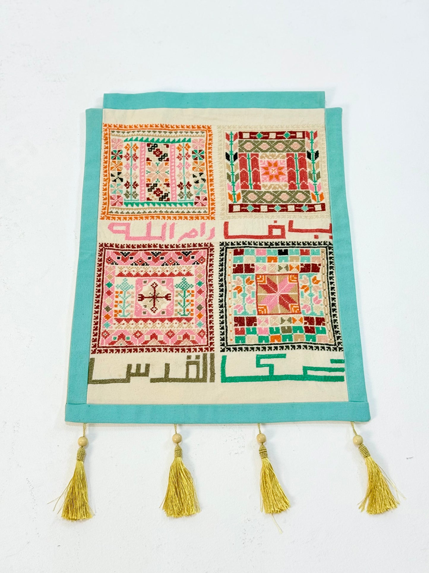 Handmade tatreez wall hanging with embroidered Palestinian city names and colorful geometric motifs on fabric, crafted by women artisans.