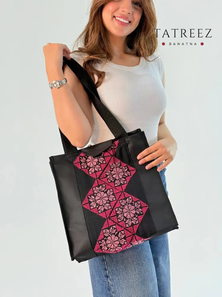 Handmade black and pink tote bag made from burlap, featuring geometric and floral embroidery, showcasing a blend of traditional and modern styles.