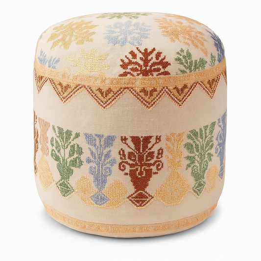 Handmade embroidered ottoman cover with traditional Palestinian tatreez patterns in beige, blue, green, and rust, crafted by women artisans in Palestine and Jordan, preserving heritage while supporting their livelihoods.