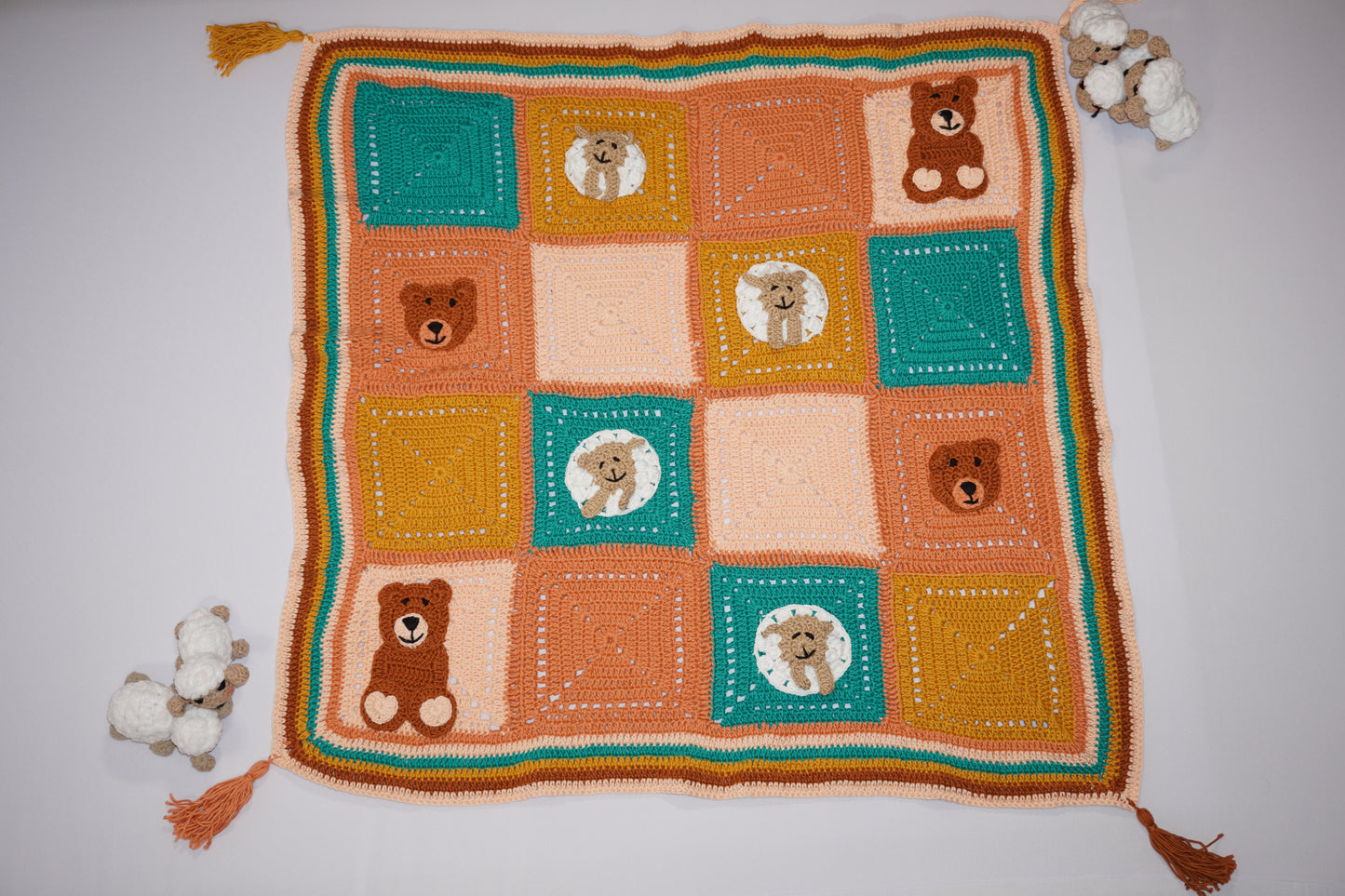 Handmade crochet baby blanket featuring playful bear and sheep faces on colorful squares in orange, green, and cream, crafted by women artisans in Lebanon, and Syria to support their livelihoods.