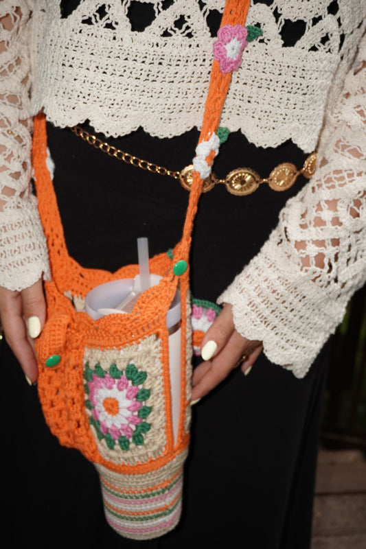 Handmade crochet Stanley bottle cover in orange with flowers, featuring green and white accents, a pocket, and a hand strap, designed for 30oz bottles.Feel free to modify any part to better fit your style!
