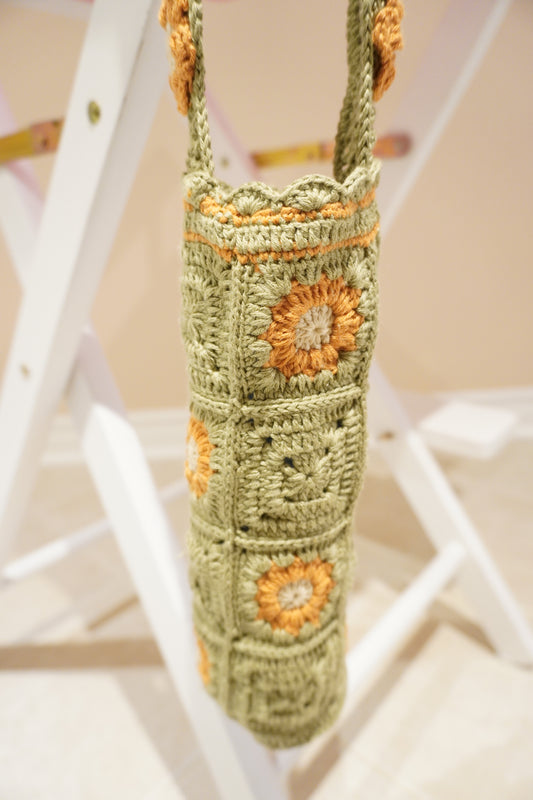 Handmade crochet bottle holder in olive green Alize cotton with orange and beige flowers, 11x26 cm size with 108 cm strap – sustainable, artisan-made accessory