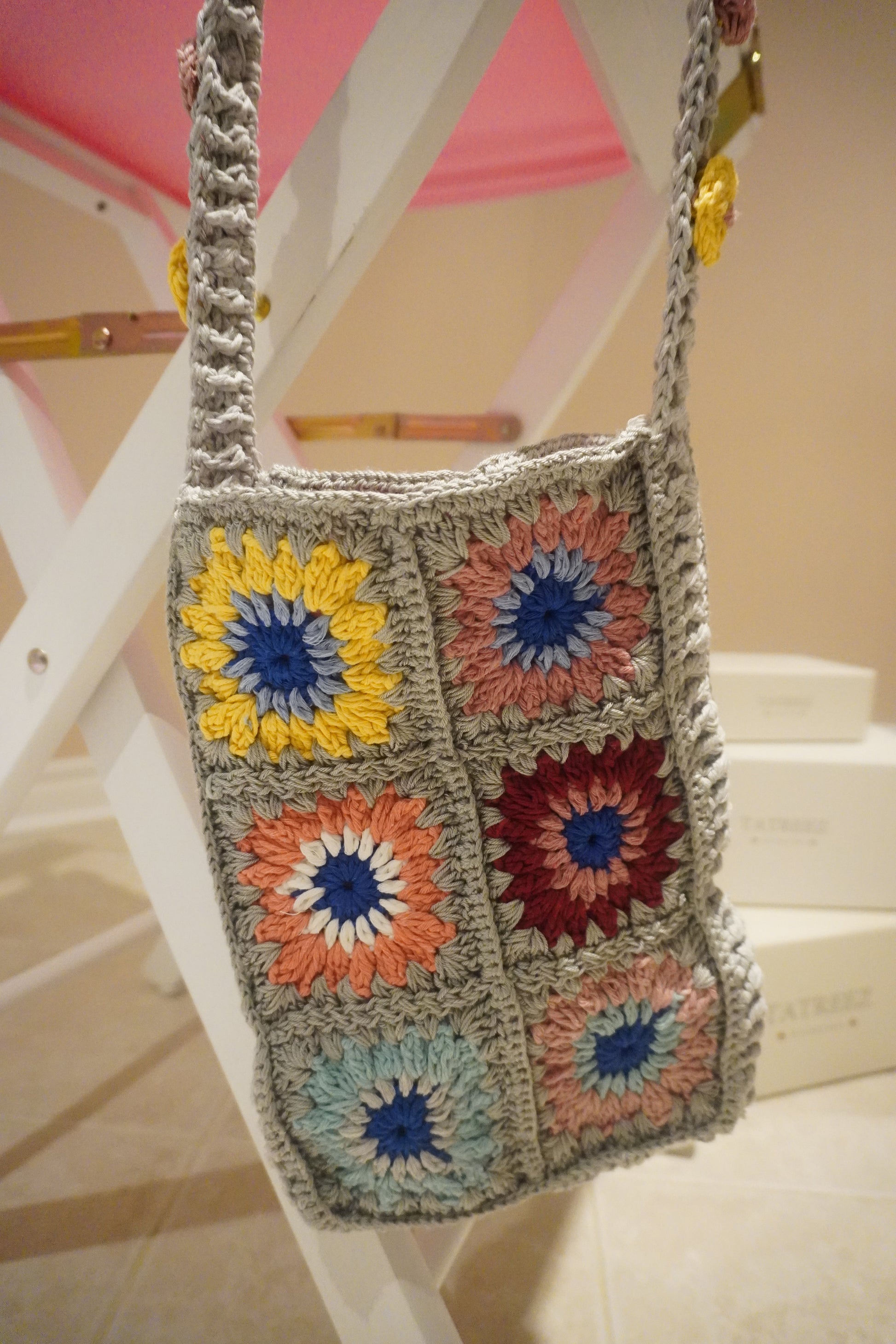 Handmade crochet messenger bag made of Alize cotton with light grey base, colorful flowers in navy blue, peach, yellow, and burgundy, measuring 120 cm x 21 cm x 30 cm, featuring pink lining and magnet clip