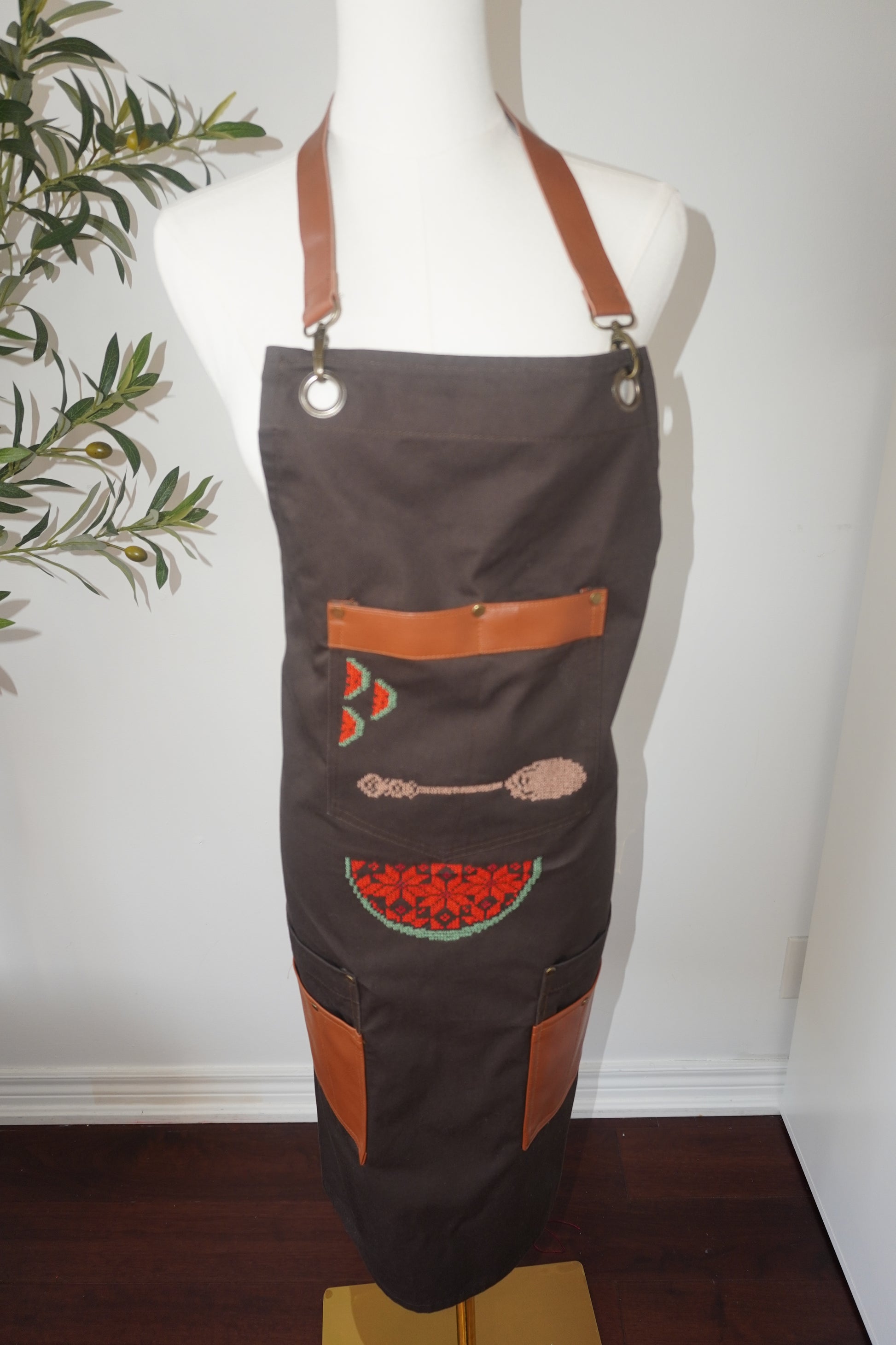 Brown apron with spoon and watermelon slices embroidered on the pocket and a colorful watermelon design on the lower part, perfect for kitchen or barbecue gatherings."