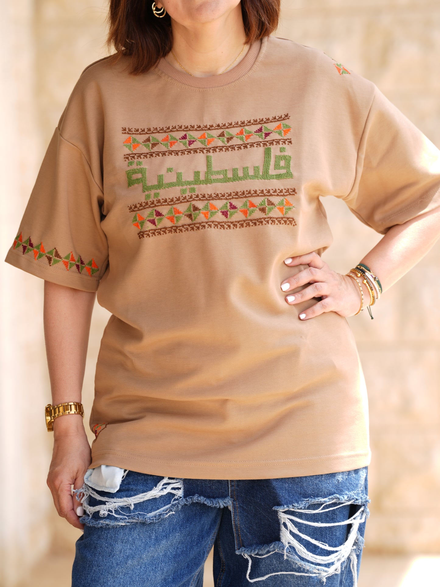 Beige cotton t-shirt with hand-embroidered Palestinian tatreez design, featuring “فلسطينية” and floral patterns, cultural heritage wear for women