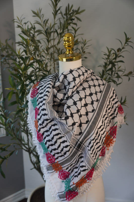 A handmade black and white kofea adorned with intricate tatreez embroidery in vibrant light green, pink, and orange, showcasing exceptional craftsmanship and a blend of traditional and contemporary style.
