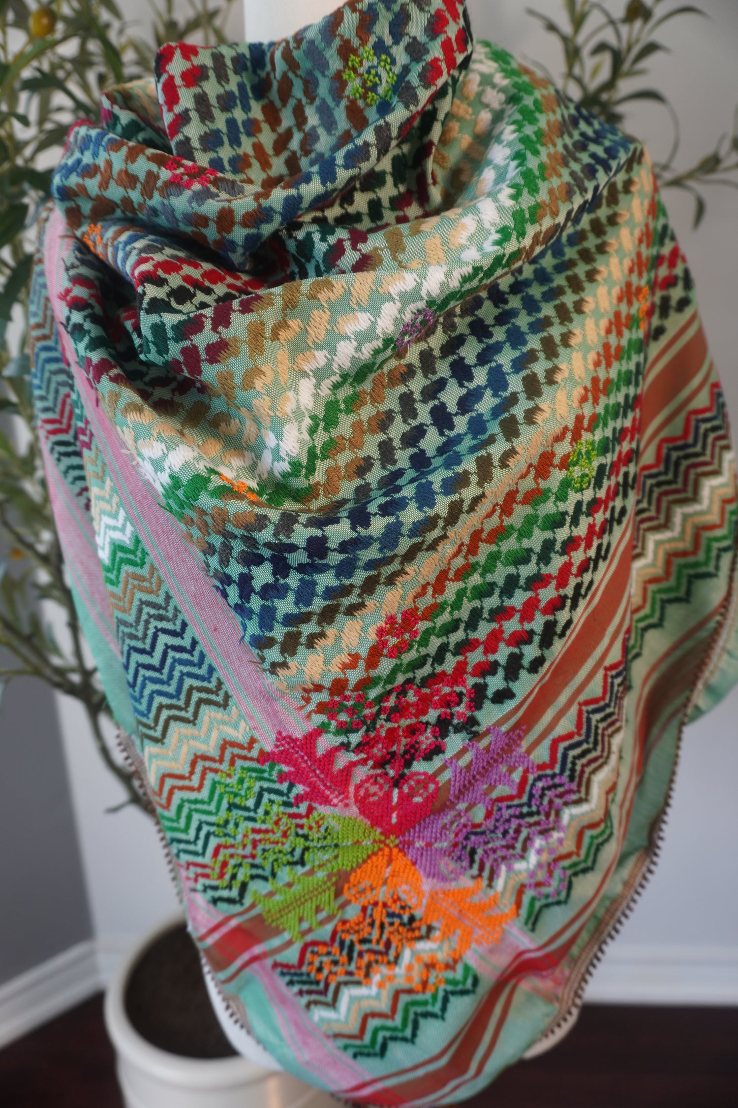 A vibrant green kofea adorned with colorful hand embroidery in shades of pink, blue, red, and brown, highlighting the intricate craftsmanship and artistic detail of the piece."