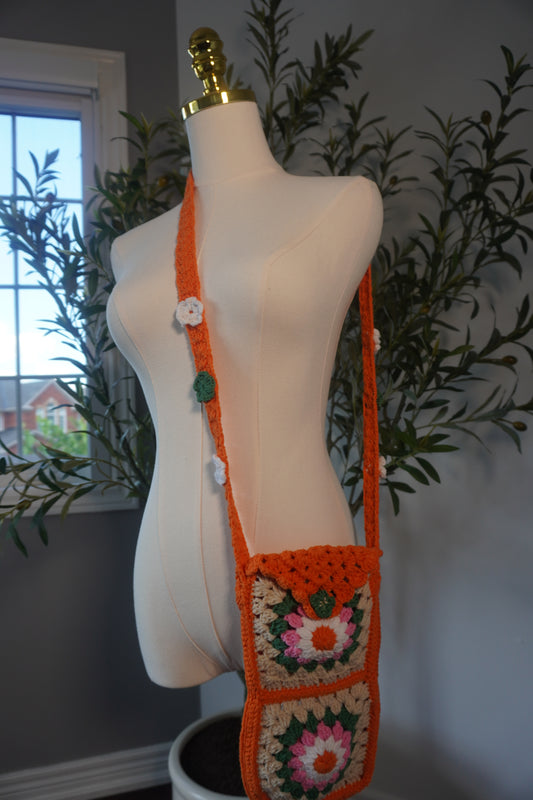 Handmade crochet phone case featuring a vibrant design of flower granny squares in shades of orange, pink, white, and beige. The case is designed for everyday use and includes a long strap for easy carrying.