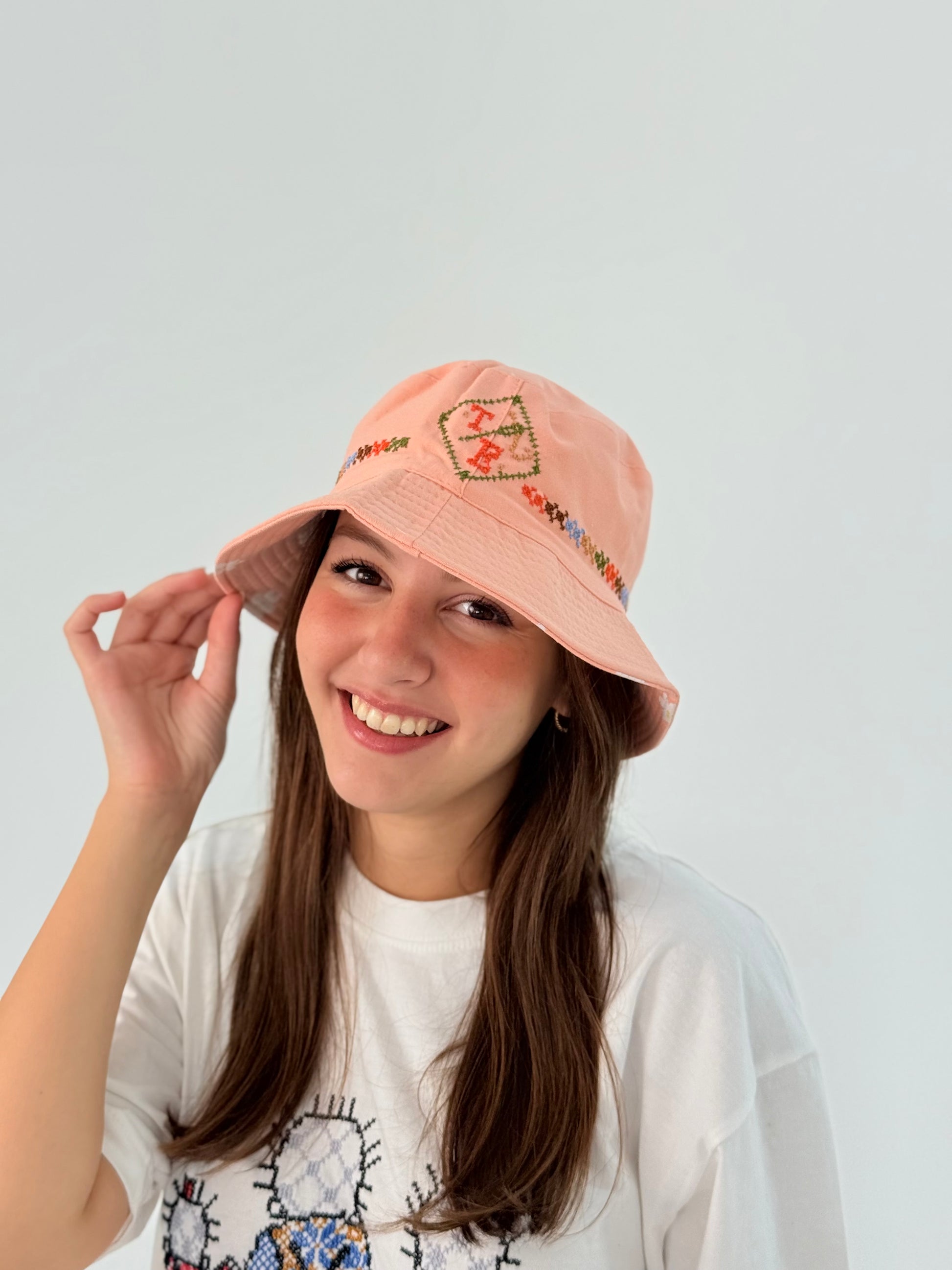 Handmade peach bucket hat with TB logo and simple tatreez embroidery.