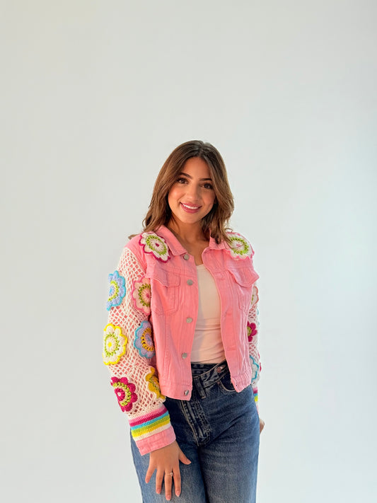 Pink jeans jacket with crochet work on the sleeves and floral accents on the front pockets, showcasing a stylish and feminine design.