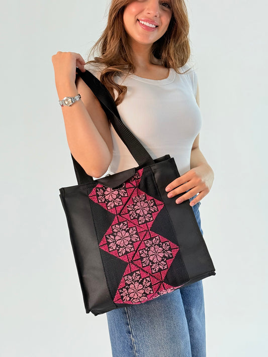 Handmade black and pink tote bag made from burlap, featuring geometric and floral embroidery, showcasing a blend of traditional and modern styles.