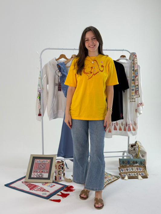 Yellow cotton t-shirt with handmade red “Palestine” embroidery, worn with jeans, supporting Palestinian artisans