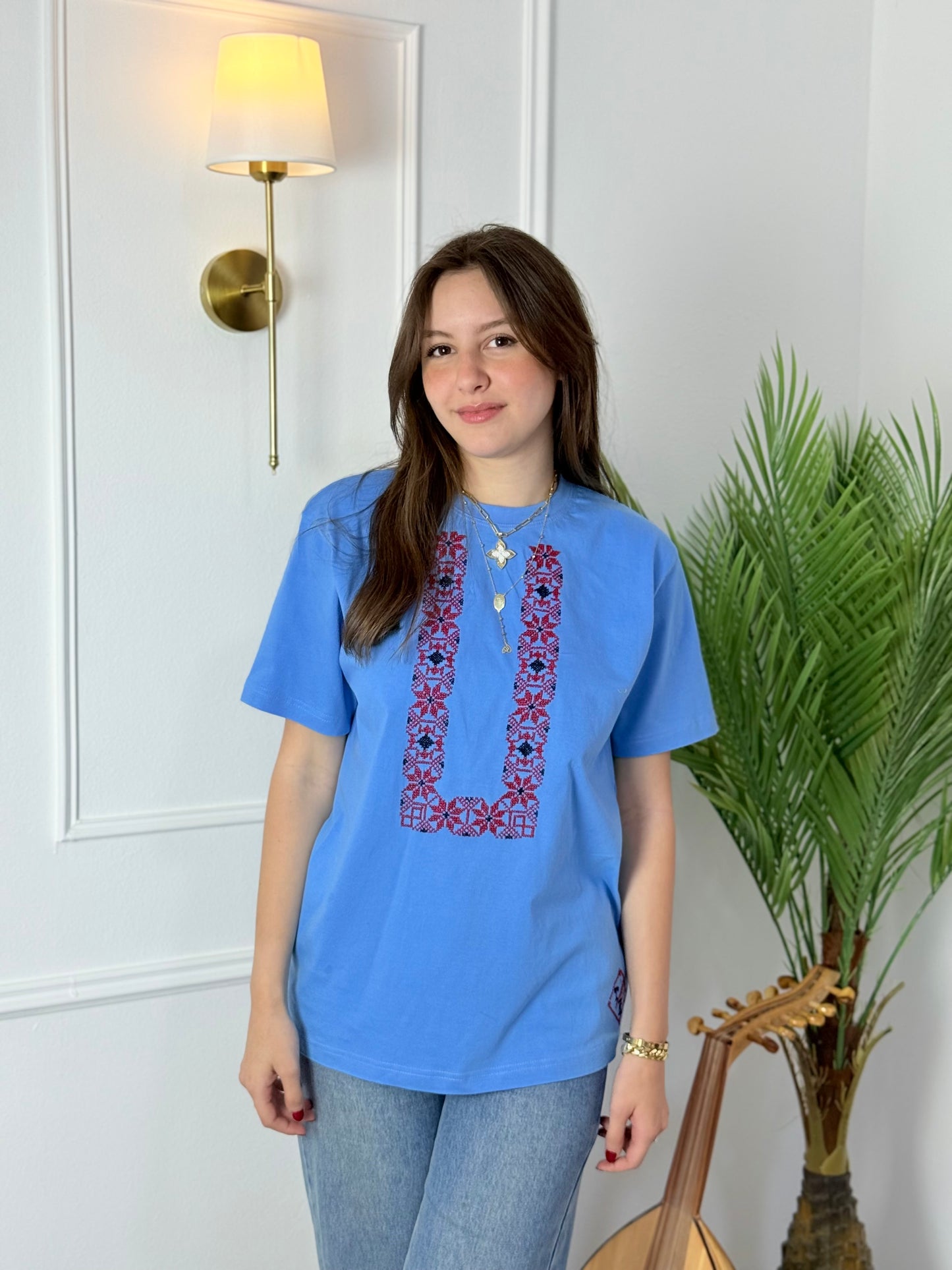 Cotton t-shirts in light blue and pink with U-shaped Palestinian tatreez embroidery, modeled with jeans, handmade by women artisans