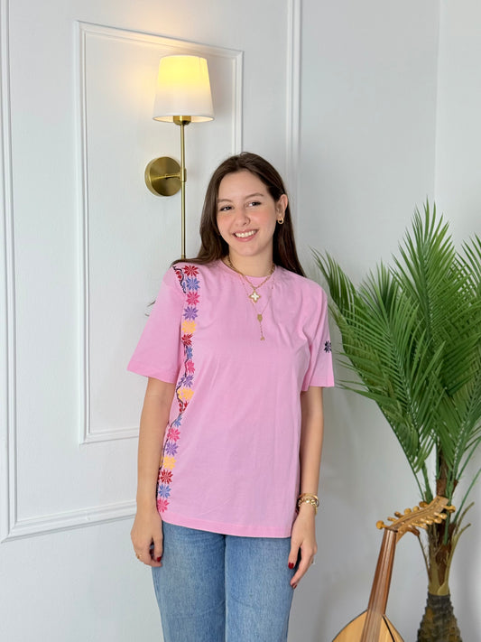 Light pink cotton t-shirt with Palestinian tatreez embroidery on the sleeve and side, modeled with jeans, handmade by women artisans