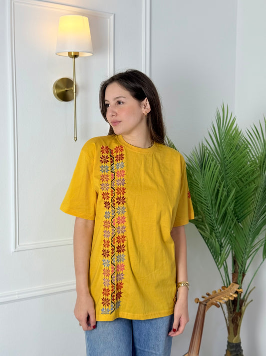 Yellow cotton T-shirt with handmade floral embroidery, crafted by Palestinian women artisans, featuring traditional tatreez design.