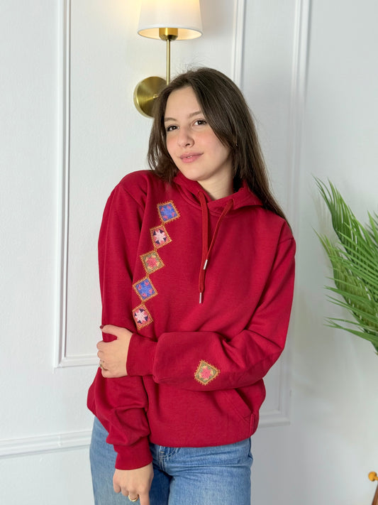 Red cotton hoodie with colorful hand-stitched Palestinian tatreez embroidery along the side and sleeve, modeled by a woman, handmade by women artisans
