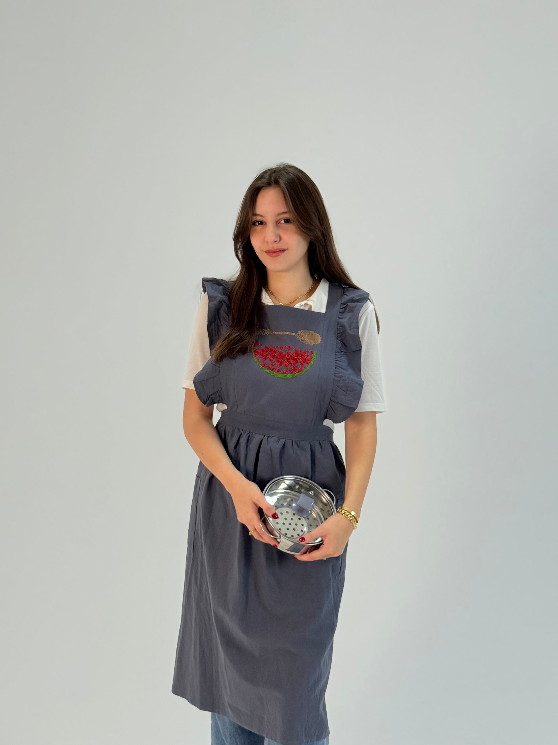 Grey apron with hand-embroidered watermelon and spoon motif, handmade by women artisans in Palestine and Jordan.
