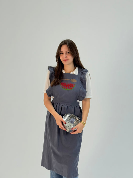 Grey apron with hand-embroidered watermelon and spoon motif, handmade by women artisans in Palestine and Jordan.
