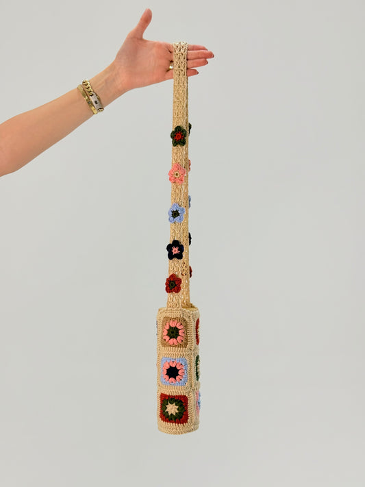 Hand-crocheted bottle cover in floral granny square pattern with beige, pink, blue, and multicolor details, made by Palestinian and Jordanian women artisans seeking financial independence while preserving regional craft heritage.