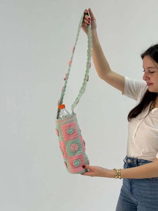 Handmade light teal and peach crochet bottle cover with geometric block design, crafted by Palestinian and Jordanian women artisans, eco-friendly reusable bottle holder.