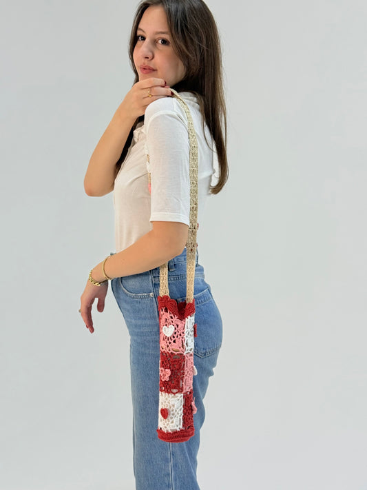 Hand-crocheted bottle cover in pink, red, and white with heart and butterfly granny square patterns, made by Palestinian and Jordanian women artisans working for financial independence while preserving crochet heritage