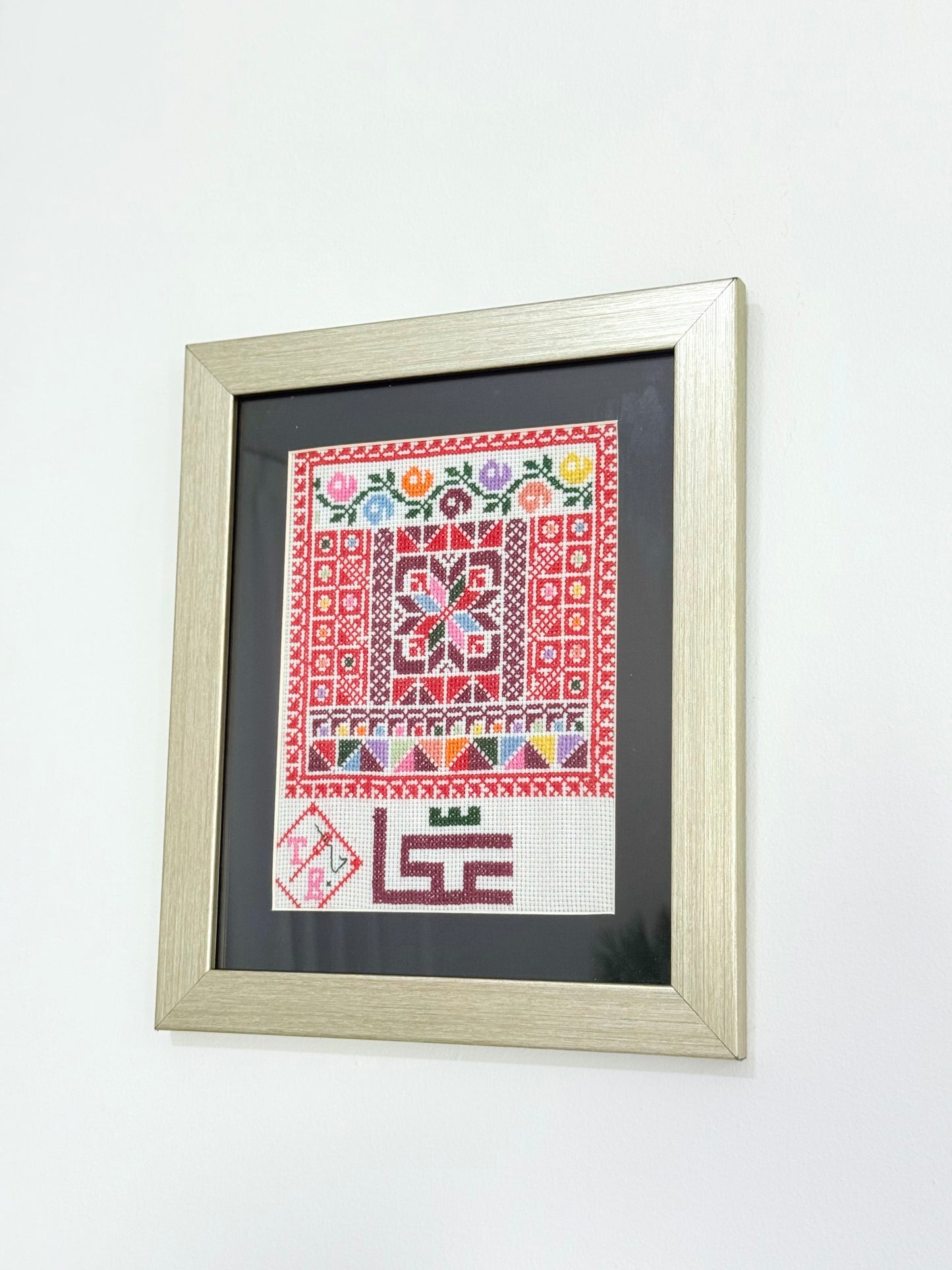 Handmade framed embroidery wall art featuring Akka city design in vibrant red patterns, crafted by Palestinian women artisans.