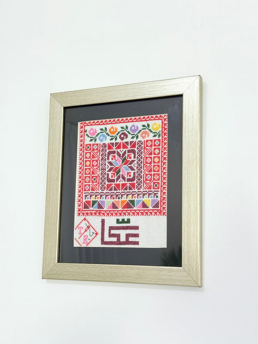 Handmade framed embroidery wall art featuring Akka city design in vibrant red patterns, crafted by Palestinian women artisans.