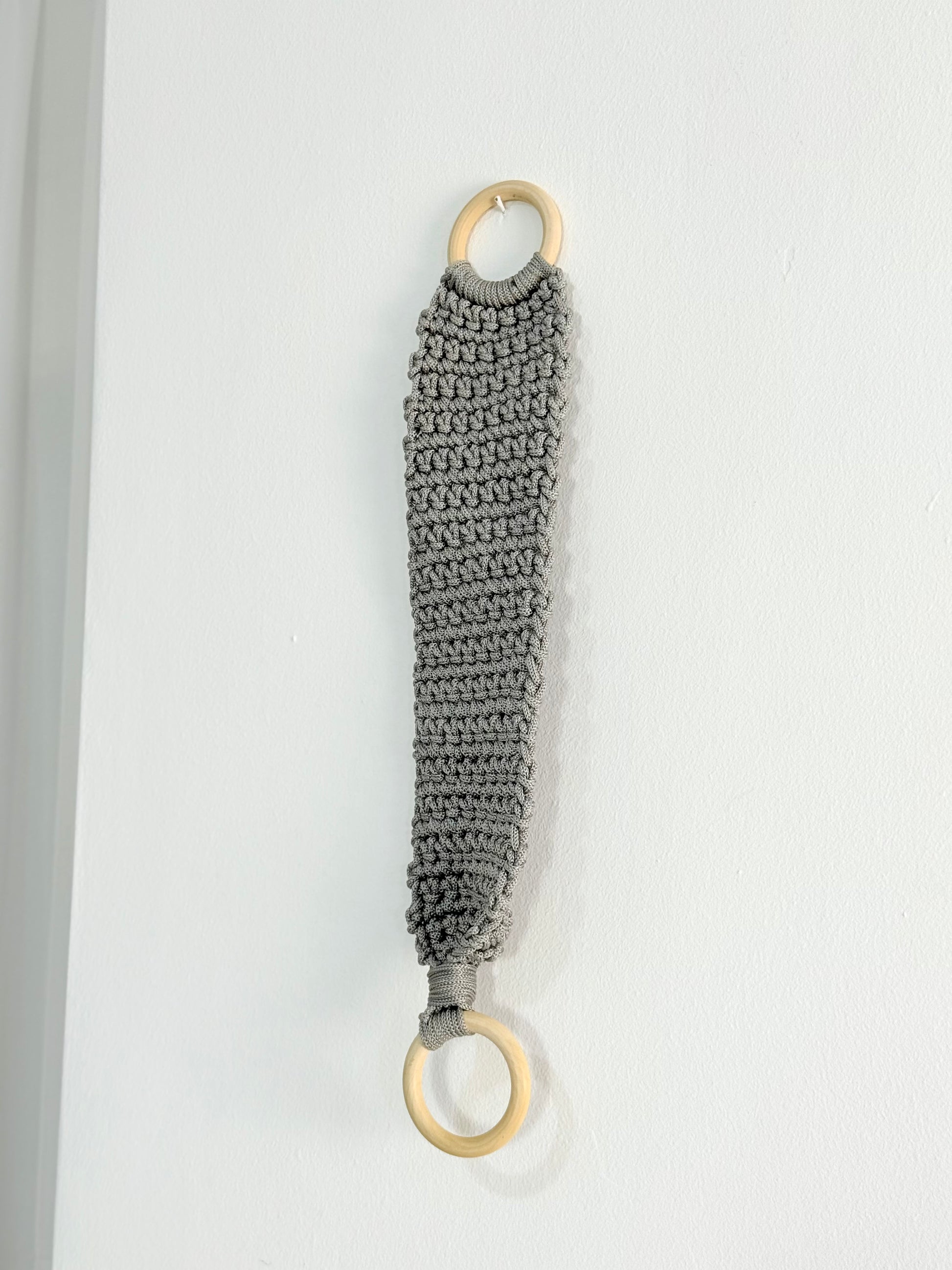 Handmade crochet kitchen towel hanger in soft grey with wooden rings, crafted by Palestinian women artisans for boho kitchen decor.