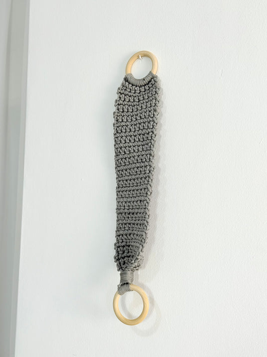 Handmade crochet kitchen towel hanger in soft grey with wooden rings, crafted by Palestinian women artisans for boho kitchen decor.