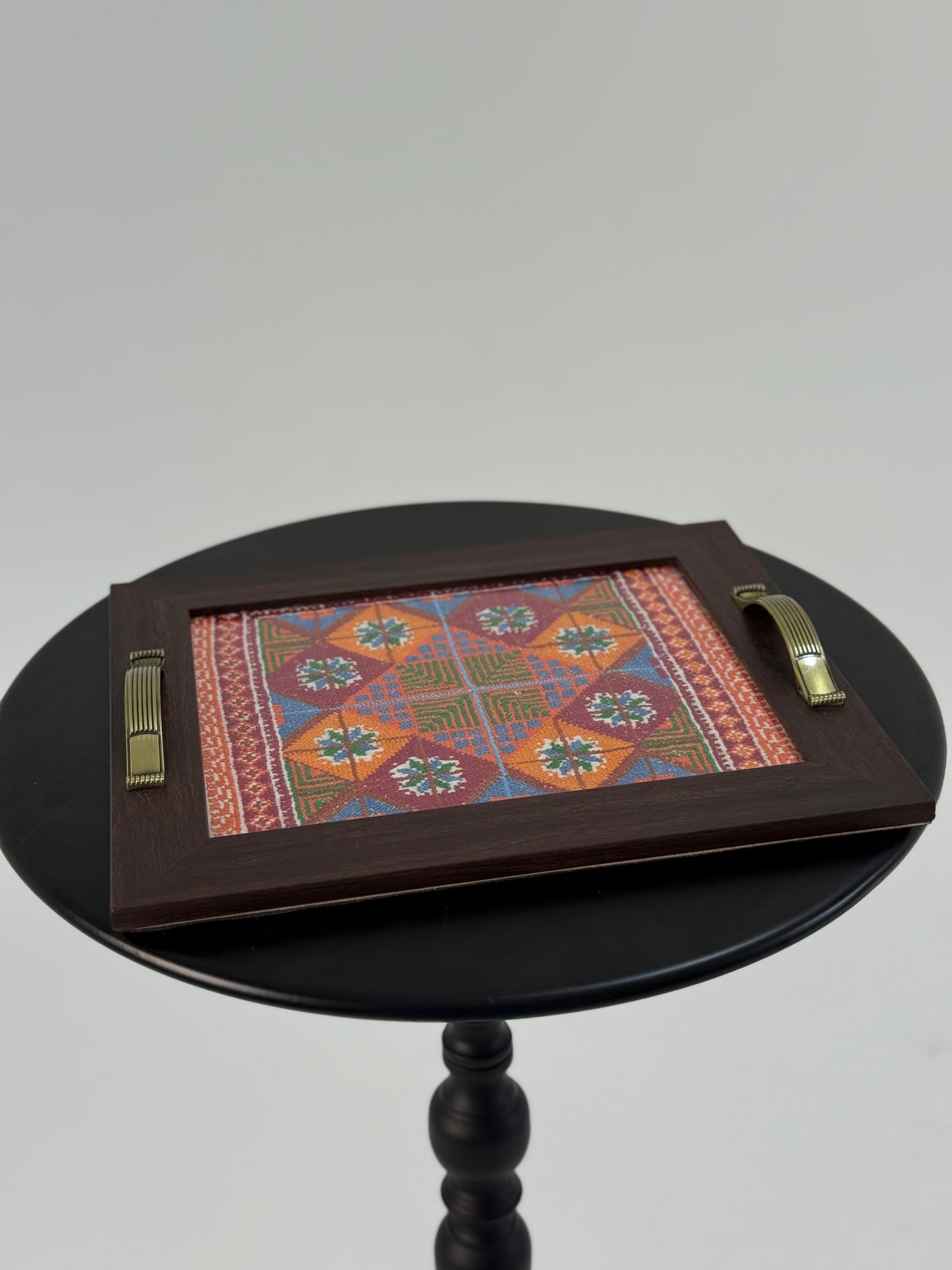 Handmade wooden serving tray with hand-stitched floral and geometric embroidery in vibrant colors, crafted by Palestinian women artisans.