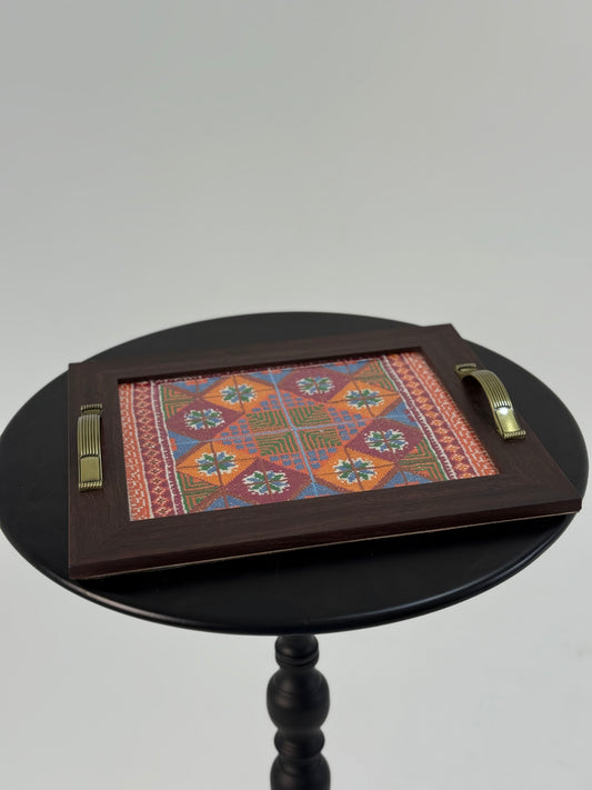 Handmade wooden serving tray with hand-stitched floral and geometric embroidery in vibrant colors, crafted by Palestinian women artisans.