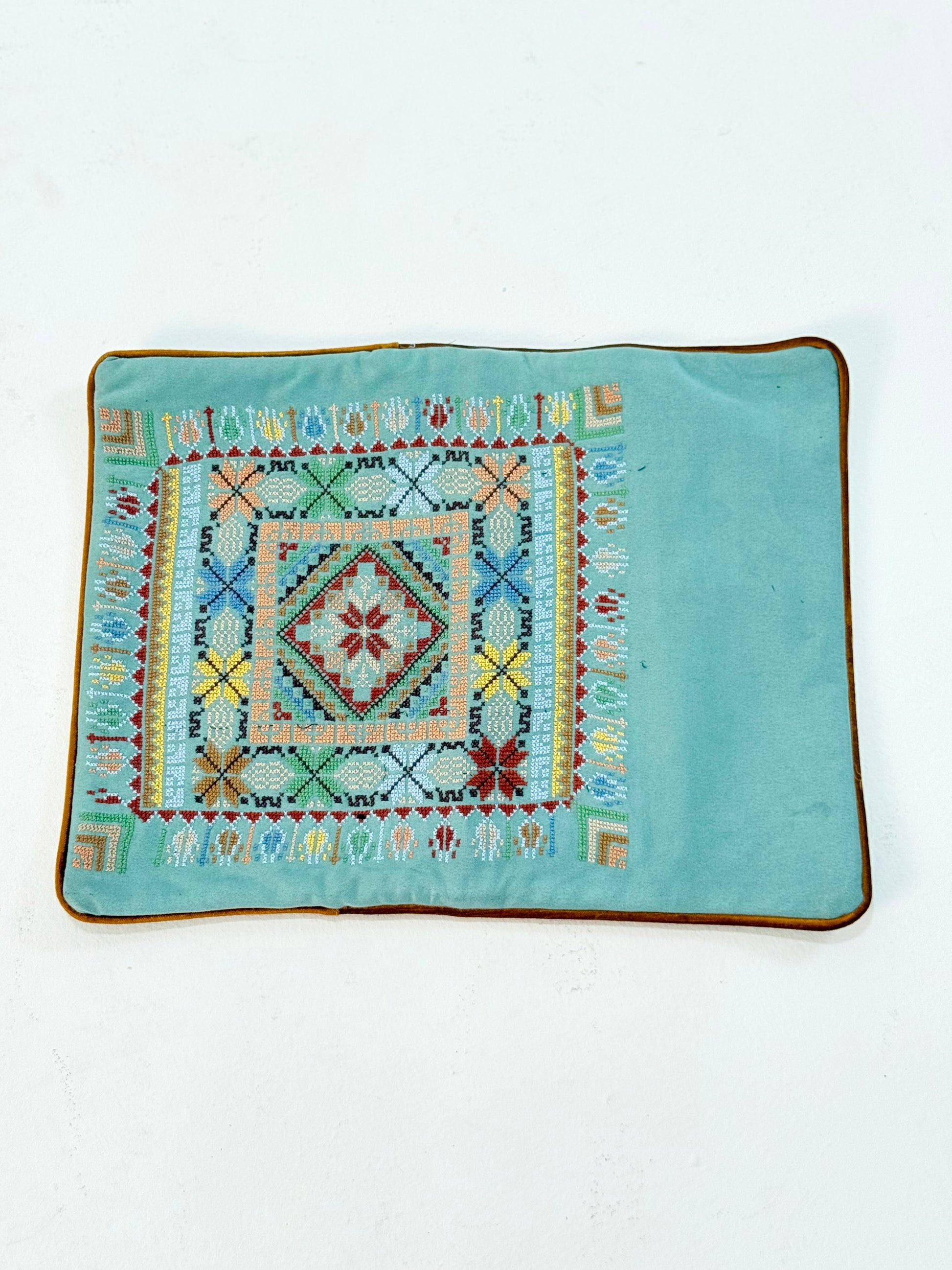 Hand-embroidered rectangular cushion covers featuring vibrant Palestinian tatreez geometric motifs on beige and turquoise backgrounds, crafted by women artisans from Palestine and Jordan to preserve heritage and support their livelihoods.