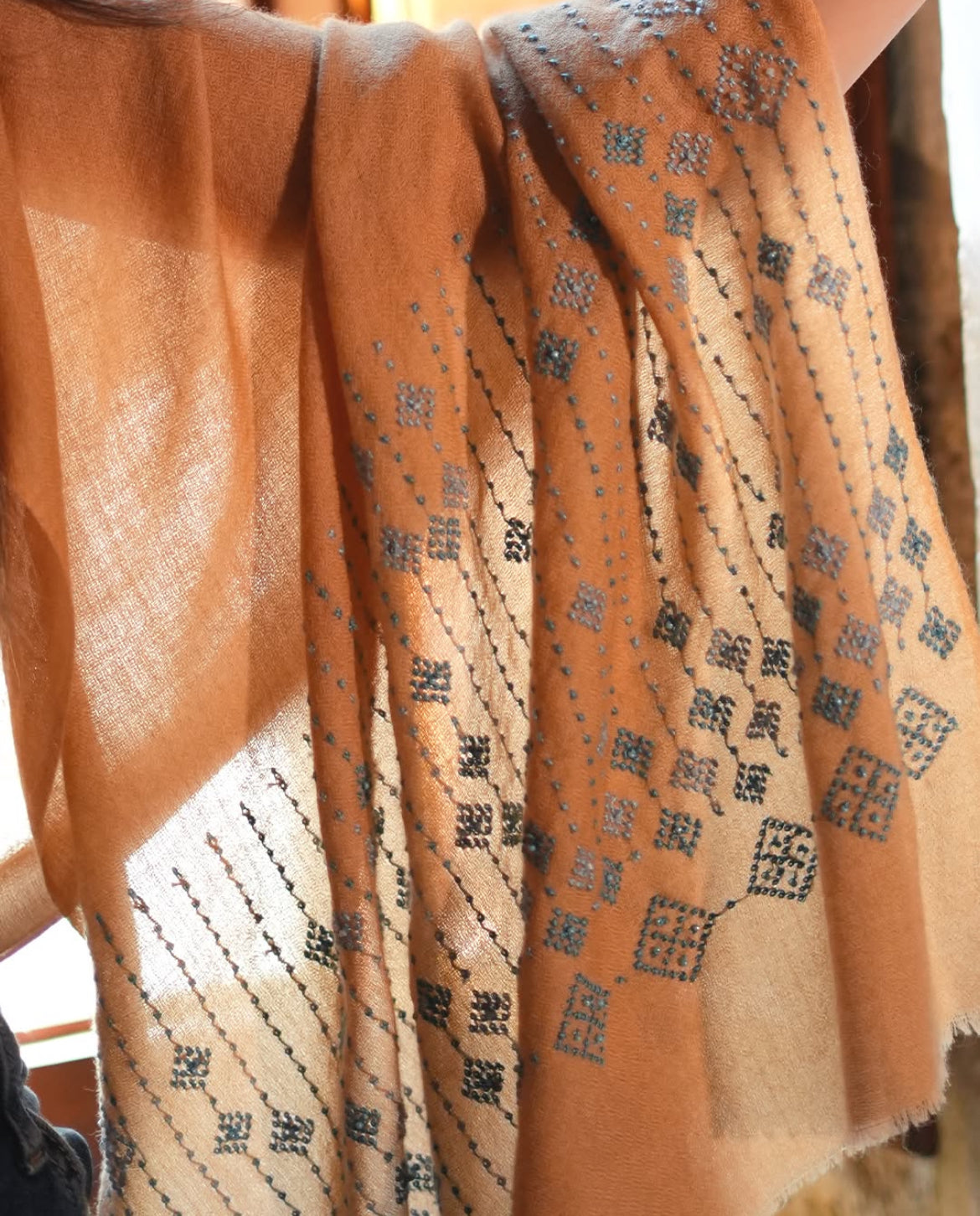 Camel-colored pashmina shawl with traditional black embroidery, handmade by women artisans.
