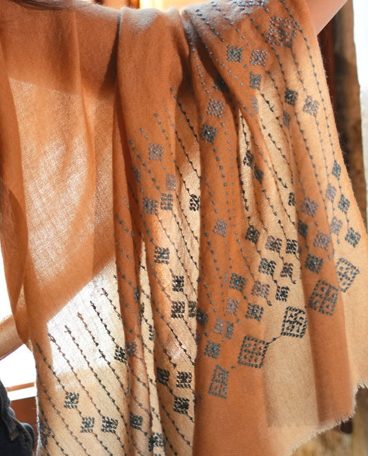 Camel-colored pashmina shawl with traditional black embroidery, handmade by women artisans.
