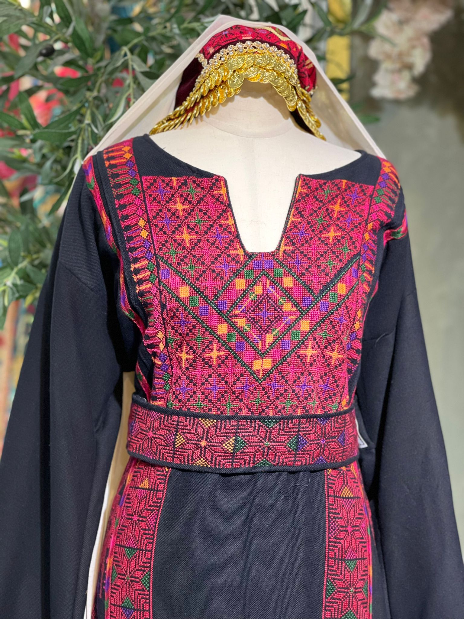 Black thoub from Yata Al Khalil with vibrant Palestinian embroidery in red, pink, green, orange, and purple. Includes a shawl with sharasheeb and two belts, one plain silk and one embroidered.