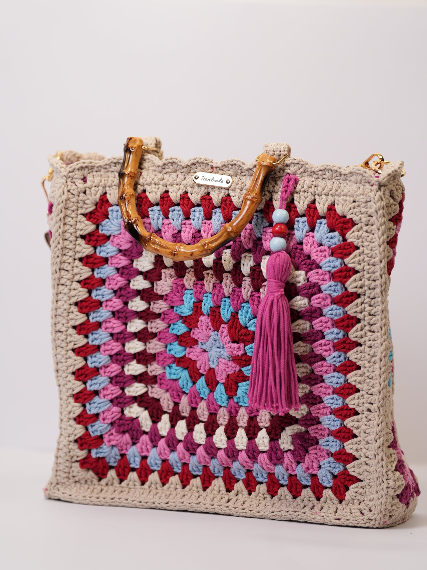 Handmade crochet granny square bag in pink, beige, and blue tones with bamboo handles and tassel, limited edition artisan handbag
