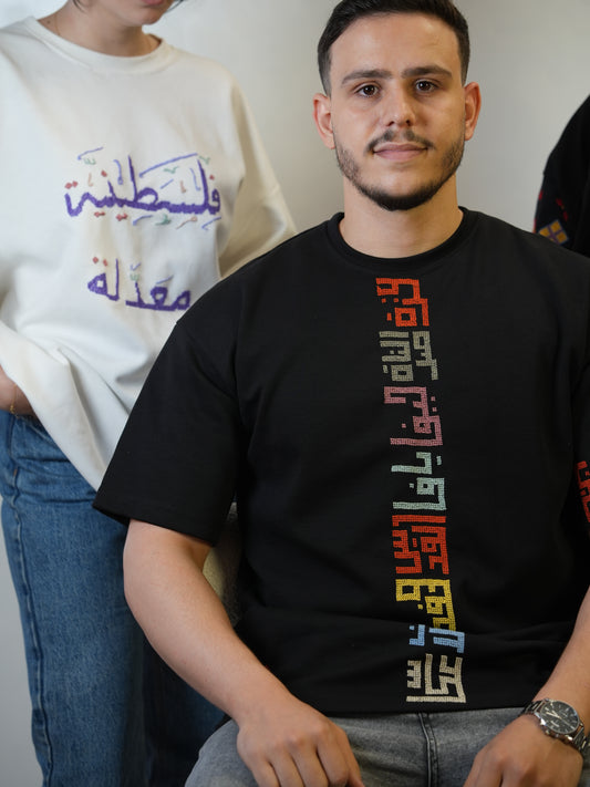 Black cotton t-shirt hand-embroidered with colorful Palestinian city names in geometric tatreez, unisex cultural heritage wear