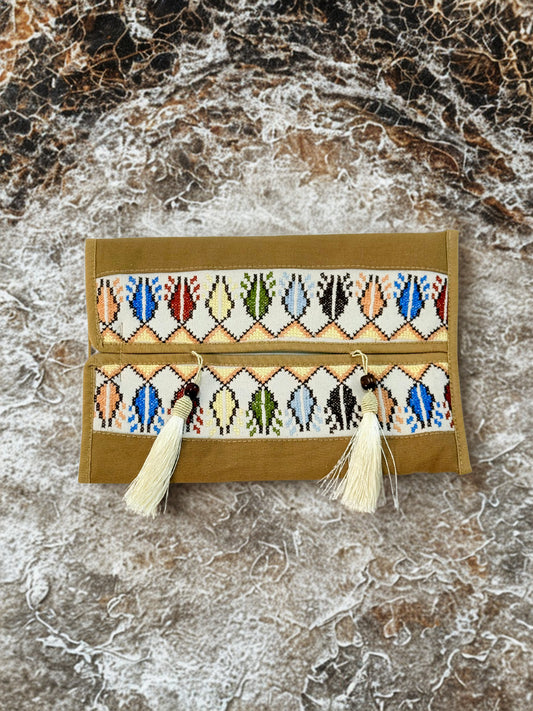 Hand-embroidered suede tissue box covers with vibrant Palestinian tatreez geometric patterns and tassel details, adding warmth and elegance to living spaces, handmade by women artisans from Palestine and Jordan. 