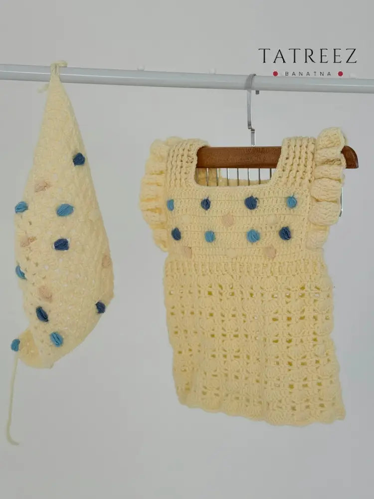 Handmade beige crochet baby dress with matching bandana, featuring blue pom-poms, crafted by women artisans for a soft, breathable fit.
