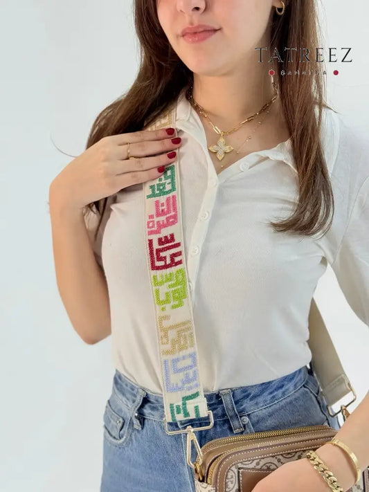 Adjustable handmade bag strap with colorful Palestinian tatreez embroidery of city names on cream fabric