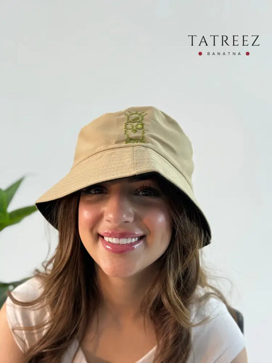 Beige bucket hat with olive green hand embroidery of the Handhala design, showcasing handmade craftsmanship and modern style.