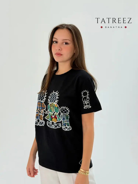 Black cotton T-shirt with Handhala family embroidered in beige, green, and yellow, featuring iconic pose on the sleeve and brand logo.