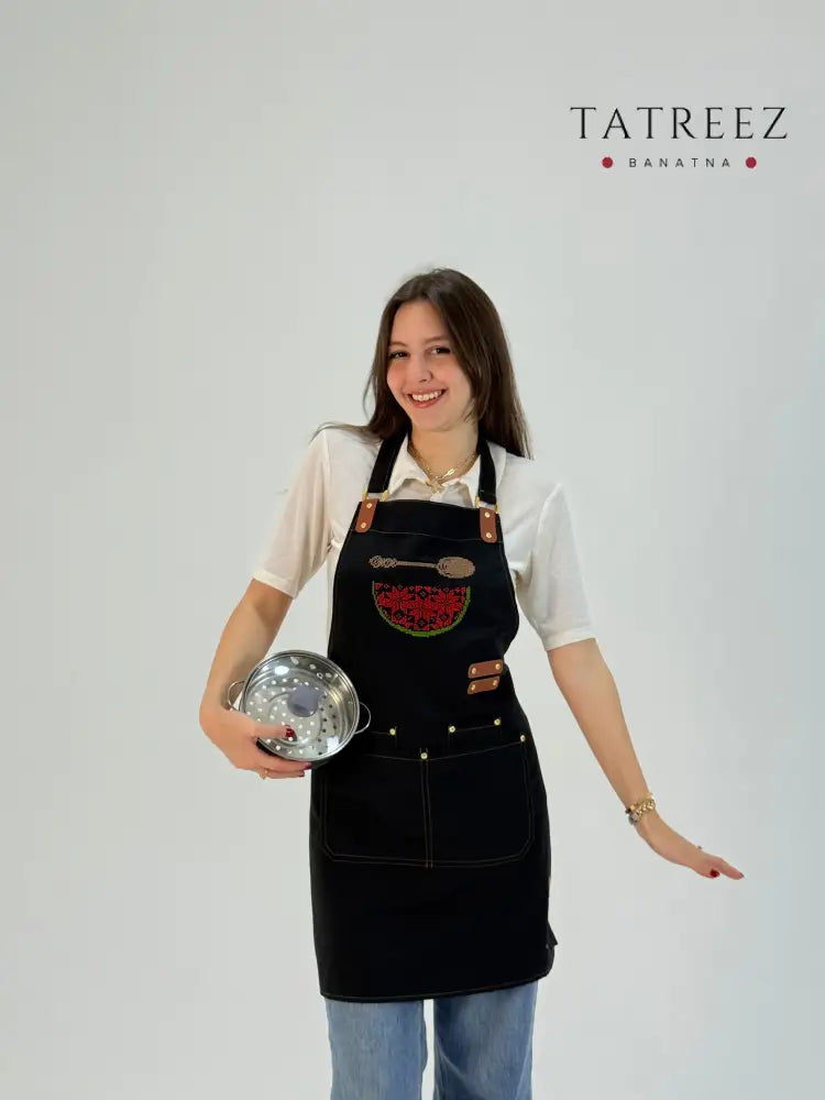 Black waterproof apron with hand-embroidered watermelon map design, made by women artisans.
