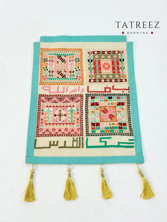 Handmade tatreez wall hanging with embroidered Palestinian city names and colorful geometric motifs on fabric, crafted by women artisans.